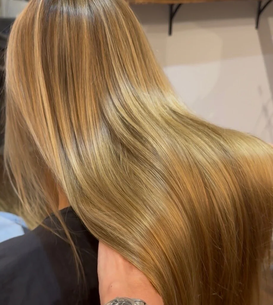 Long, glossy golden blonde hair with soft highlights, seen from the back in the salon